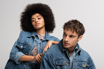 brunette african american woman looking at camera and leaning on man in denim outfit isolated on...