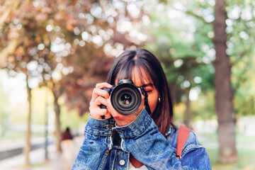 Casual woman taking photo on camera. Unrecognizable female photographer in denim jacket taking picture on photo camera while standing in green park in daylight