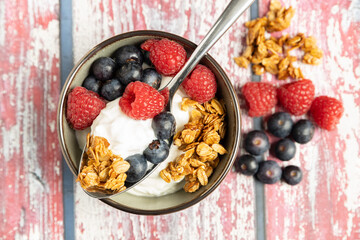 yogurt with crunchy granola and raspberries and blueberries in a bowl on a wooden background