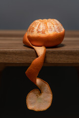 Partially peeled tangerine on a wooden table and dark background. Selective focus.