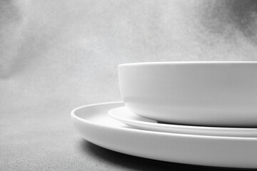 Stack of white porcelain plates and bowls on neutral gray background. copy space