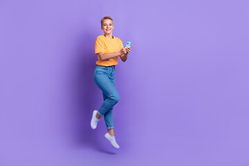 Fototapeta na wymiar Full size photo of excited cheerful girl jumping hold smart phone empty space isolated on violet color background