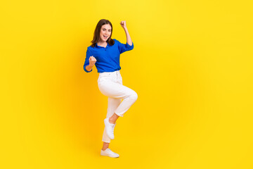 Fototapeta na wymiar Full length photo of charming lucky girl dressed blue shirt rising fists empty space isolated yellow color background