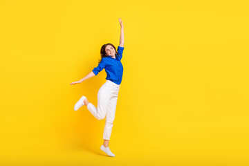 Fototapeta na wymiar Full length photo of charming sweet girl dressed blue shirt jumping high rising arms hands empty space isolated yellow color background