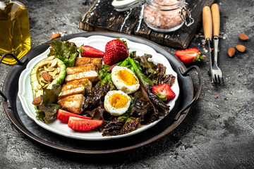 Healthy nutritious paleo keto breakfast diet two eggs, avocado, grilled chicken fillet, nuts, strawberries and fresh salad. Keto breakfast or lunch. place for text, top view
