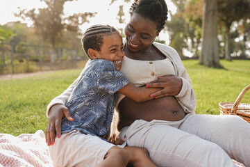 Happy african mother hugging son at city park - Pregnant woman with child outdoor - Powered by Adobe