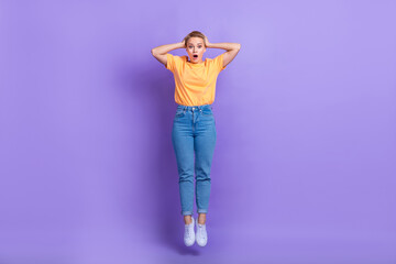 Full size photo of impressed staring girl wear yellow t-shirt denim trousers hold arms on head isolated on purple color background
