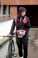 Bike courier woman walking with her bike and talking by walkie-talkie.