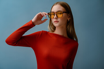 Fashionable confident woman wearing trendy orange color glasses with leopard frames, posing on blue background. Close up studio portrait. Copy, empty space for text  © Victoria Fox