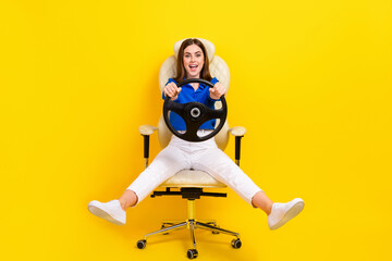 Full length photo of young overjoyed excited business lady spend free time play driving simulator steering wheel isolated on yellow color background