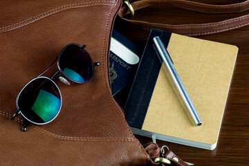 Leather Bag with Passport Sunglasses Pen and Notebook on a Polished Wooden Surface - Powered by Adobe