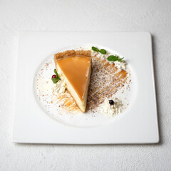 Cheesecake with caramel. Piece of dessert sprinkled with nuts and decorated with mint on plate. Sweets with salted caramel. White background. Top view. Copy space. 