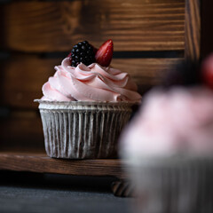 Cupcake on wooden shelf. Dessert is decorated with cream and fresh berries. Festive baking. Wooden background. Soft focus. Close-up. Side view. 
