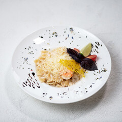 Pasta farfalle with shrimp and cheese, garnished with slice of lemon, tomato and basil leaves. Pasta in white plate on white background. Top view. Copy space.