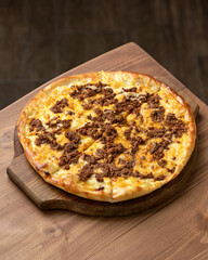 Pizza with minced meat. Pizza with cheese and meat is cut into pieces on wooden board, on wooden table. Italian cuisine. Fast food. Wooden background. Top view. Copy space. 