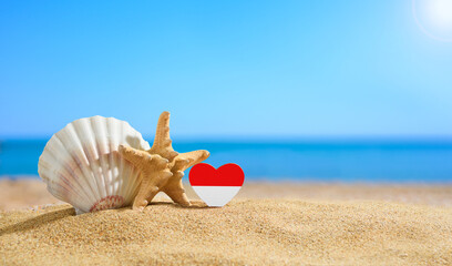 Beautiful Indonesian beach. Flag of Indonesia in the shape of a heart and shells on a sandy beach.