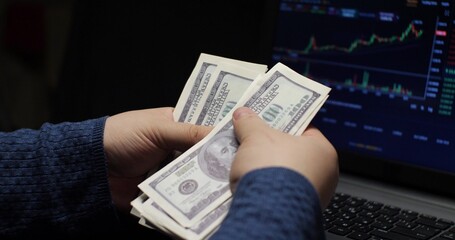 The broker is counting dollars in front of a laptop screen with a cryptocurrency chart. Dollars received by buying and selling cryptocurrencies on the spot. Cryptocurrency spot concept.