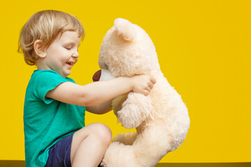 Little boy hugging teddy bear toy on yellow background