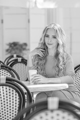 beautiful young girl drinks coffee from a cardboard cup in a cafe with wicker furniture