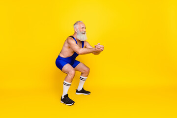 Fototapeta na wymiar Photo of active energetic sportive retired man war overall sitting up squats cardio look empty space isolated on yellow color background
