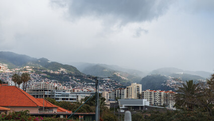 Beautiful city with houses on a background of mountains with fog and clouds on the island of Madeira.