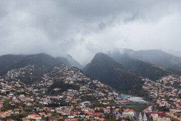 Beautiful mountains with fog, clouds and houses on Madeira island. City on the side of a mountain