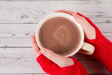 Hot chocolate on a wooden background in a cup held in woman's hands