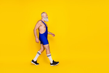 Fototapeta na wymiar Full length profile photo of sportive aged man walking look empty space isolated on yellow color background