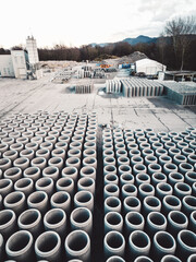 Vertical photo of construction company firm storage place with concrete pipes neatly lined up in rows on the grounds 