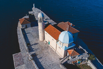 Aerial drone view of Gospa Od Skrpjela island, our Lady of the Rocks church, Montenegro, Boka Bay and Adriatic sea, with Perast town and island of Saint George in the background in a sunny day