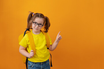back to school, cute joyful girl child 6-7 years old smiling on an isolated yellow background in with a school backpack