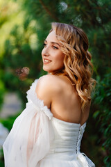 a bride in an open-shouldered dress poses against the backdrop of greenery