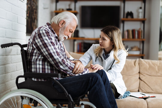 Young nurse talking with sad senior man in a wheelchair during home visit