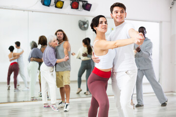 Young smiling guy learning to dance waltz paired with expressive positive Hispanic girl in dancing...