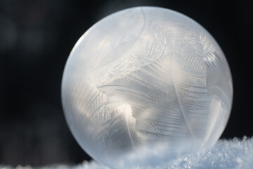 Close-up of a frozen soap bubble lying on ice crystals. The background is black with bright...