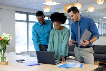 Happy diverse business people using laptop and discussing in modern office