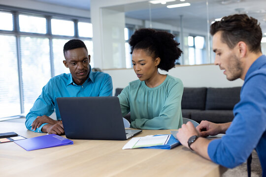 Happy diverse business people using laptop and discussing in modern office