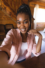 Portrait of happy african american woman spending time in log cabin and having video call