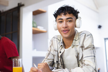 Happy biracial teenage boy with headphones sitting at desk