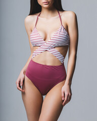 The body of a slender young girl in a fashionable swimsuit on a studio gray background. Diet, fitness, healthy lifestyle