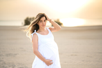 A portrait of a beautiful pregnant woman smile brightly in white dress on the beach