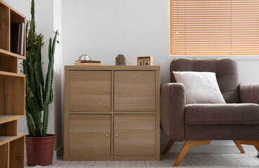 Interior of light living room with wooden drawers and armchair