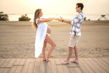 Beautiful young couple holding hands and celebrating upcoming roles of mother and father to their unborn child. Pregnant woman and handsome man at beach.
