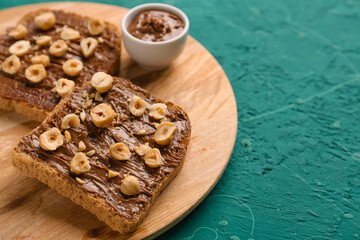 Wooden board of tasty toasts with hazelnut butter and nuts on color background, closeup
