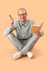 Young man in eyeglasses with disposable electronic cigarette reading book on beige background