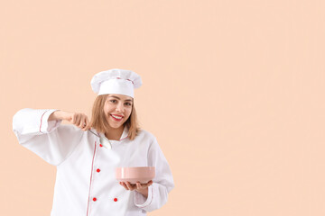Female chef with spoon and bowl on beige background