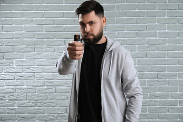 Young man with pepper spray for self-defence on grey brick background