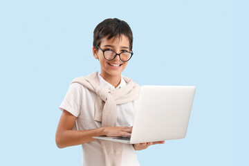 Little boy in eyeglasses using laptop on blue background