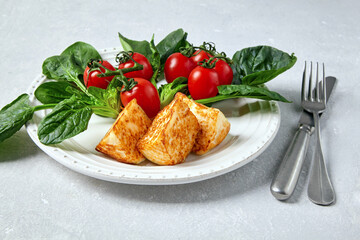 Fried curd cheese mozzarella halloumi with cherry tomatoes and green spinach on a white plate