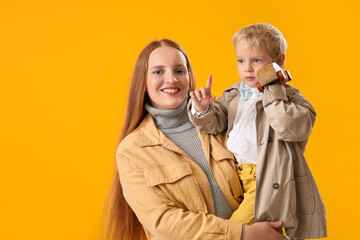 Happy mother and her little son with toy car on yellow background
